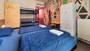 A dormitory room with bunk beds, a wardrobe, and a geometric-patterned wall.