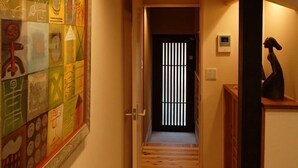 A hallway with wooden flooring, a tiled wall with colorful artwork, and a door at the end. - Gion Machiya (Kyoto)