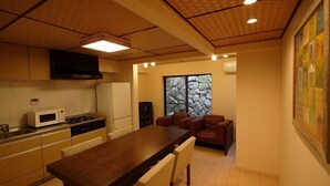 A modern kitchen with a wooden table and chairs, a microwave, and a stove. There is a stone wall and a window with a view of the outdoors. - Gion Machiya (Kyoto)