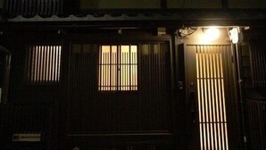 A traditional Japanese building with a dark facade, a wooden door, and a small illuminated window above the entrance. - Gion Machiya (Kyoto)