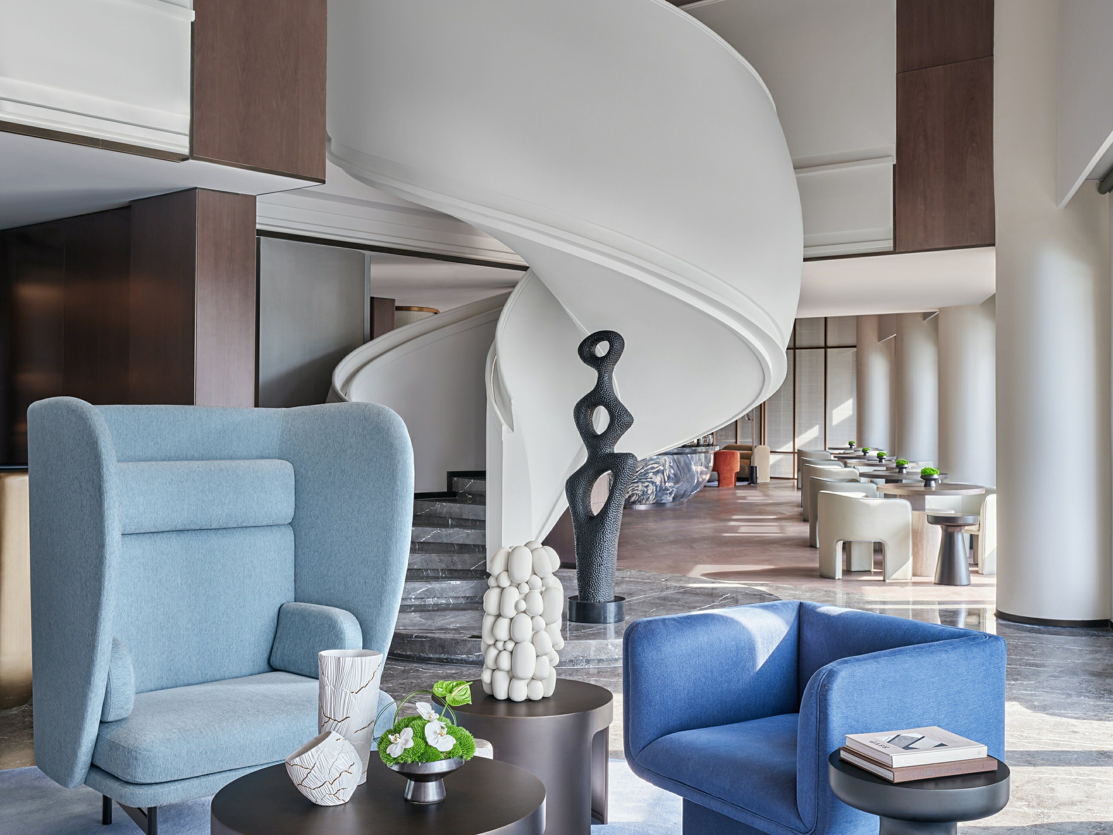 A modern lobby with a blue sofa, a coffee table, and a spiral staircase.