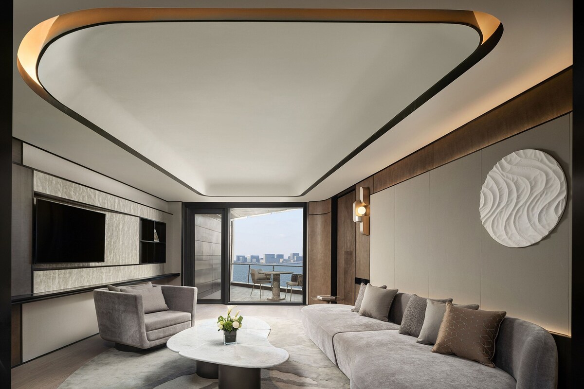 Een moderne woonkamer met een grote flatscreen televisie, een ronde salontafel en een grijze bank.