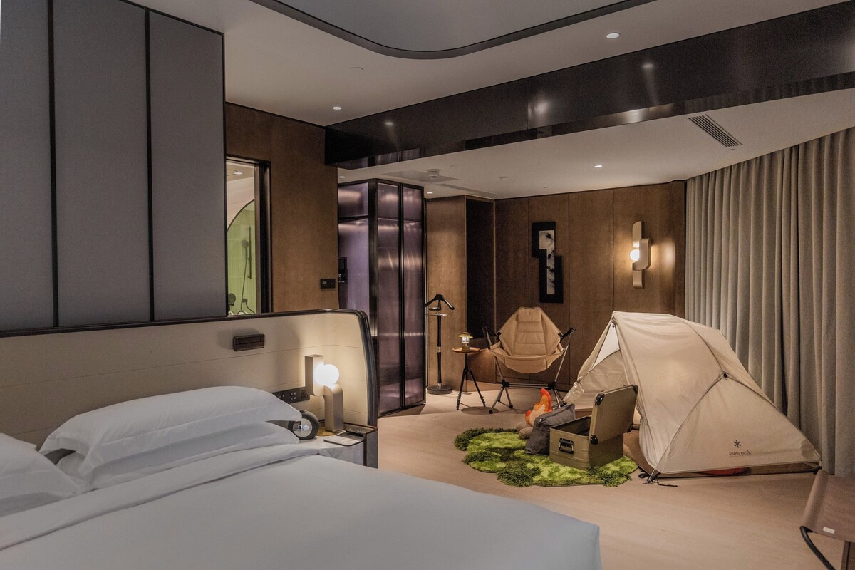 Een moderne hotelkamer met een bed, een tent, een stoel en een bureau met een laptop.