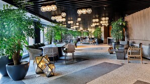 Un espacio interior moderno con zonas de estar, plantas en macetas y luces esféricas colgantes.