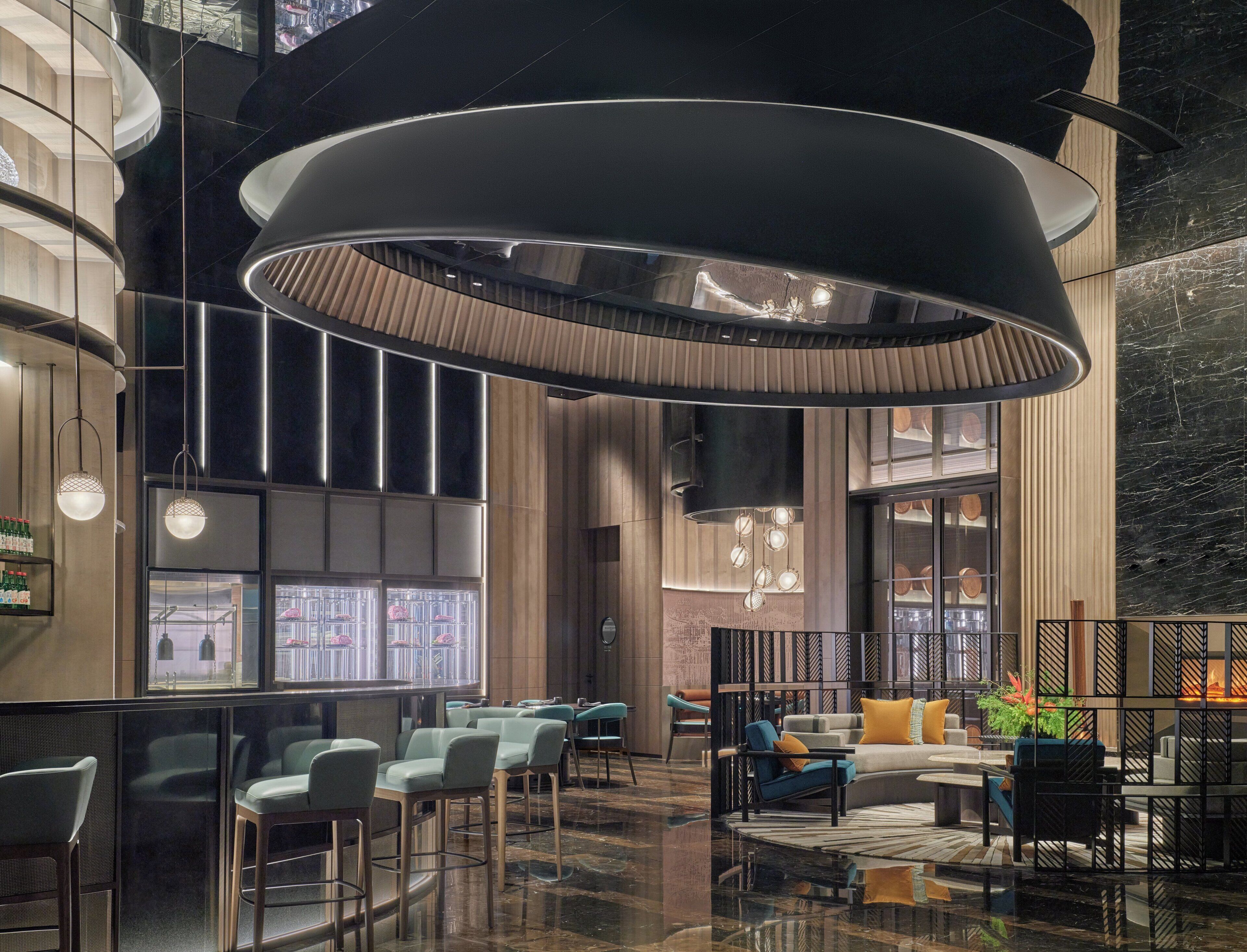 Eine moderne Lobby mit einer großen, runden Deckenleuchte, Sitzbereichen und Blick auf die Stadt durch große Fenster.