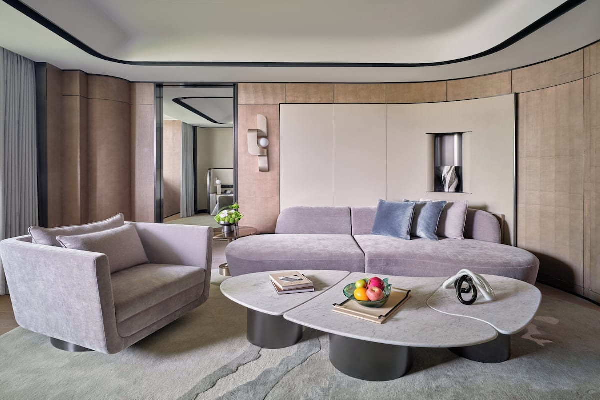 A modern living room with a grey sofa, a smaller armchair, and a coffee table with books and a fruit bowl.