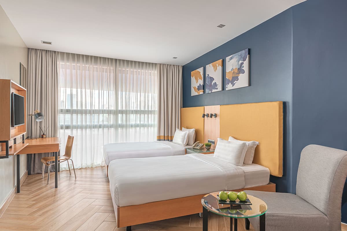 A hotel room with two beds, a desk, a chair, a glass table with apples, and a TV.