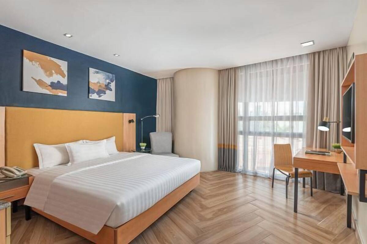 A hotel room with a large bed, a desk, a chair, a nightstand, and a lamp.
