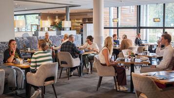 A modern dining area with multiple tables and chairs, large windows, and a central bar area.