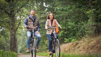 Two people riding bicycles on a paved path surrounded by trees.