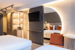 Una habitación de hotel con televisión, dos camas, una cafetera y una mesita.