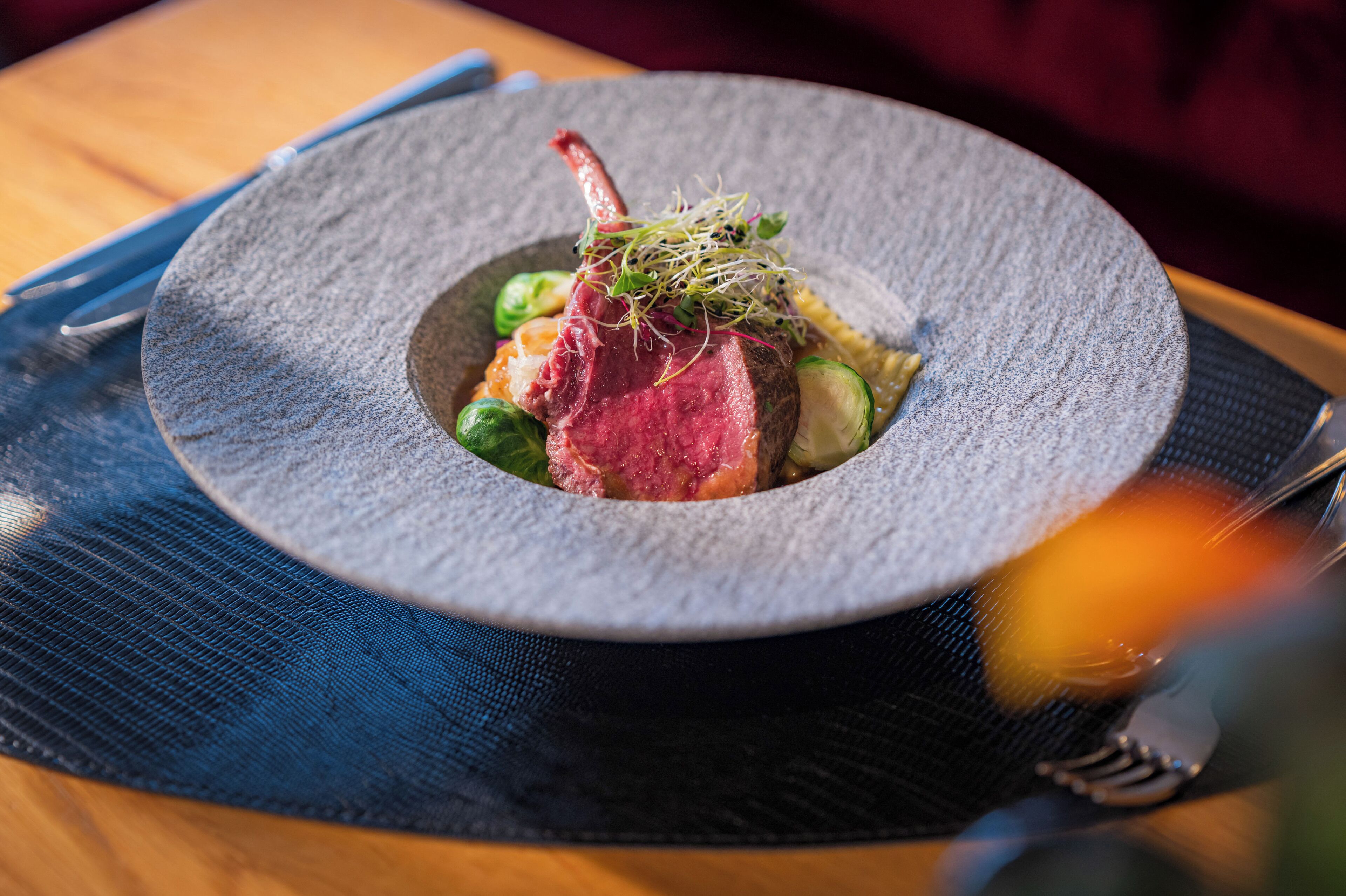 A plate of food with a meat centerpiece, garnished with greens and sprouts, on a textured plate.