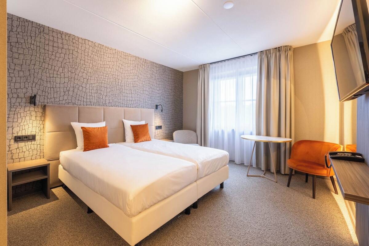 Ein Hotelzimmer mit einem großen Bett, einem Schreibtisch, einem Sessel, einem Fernseher und einem kleinen Tisch.