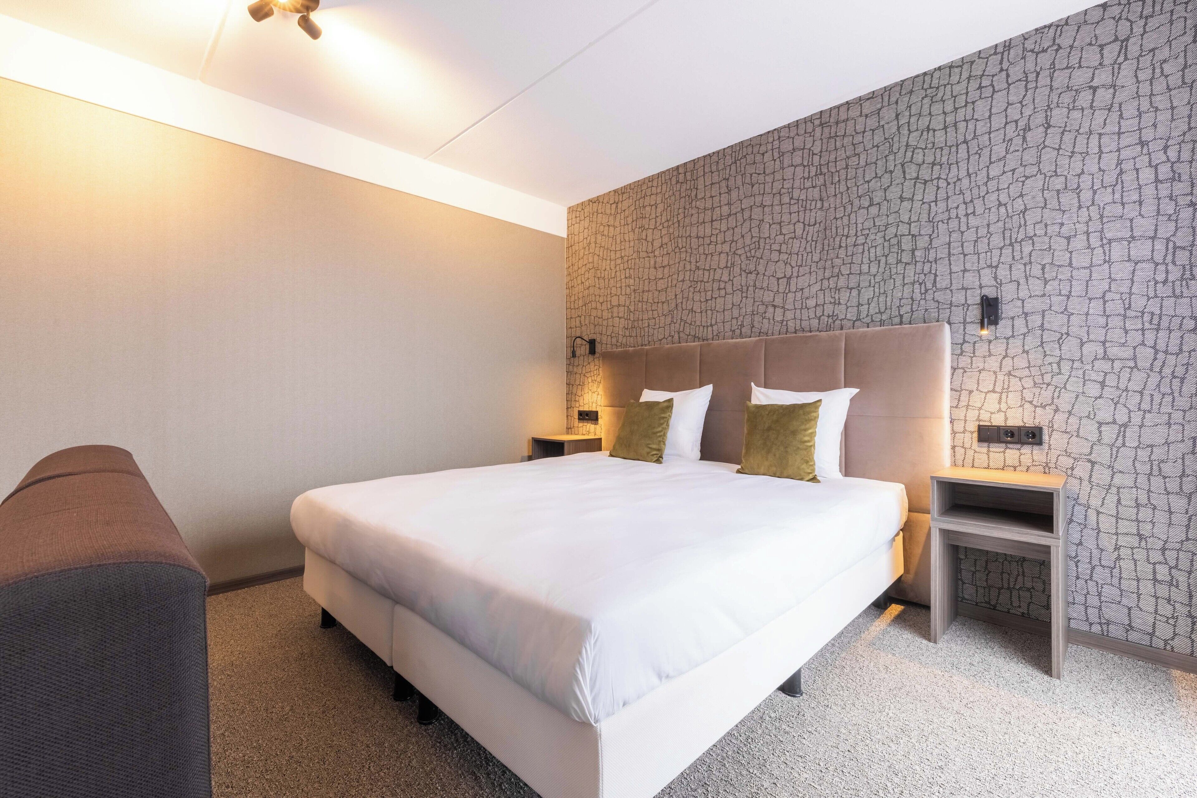 A hotel room with a large bed, a nightstand, and a wall with a textured pattern.