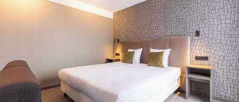 A hotel room with a large bed, a nightstand, and a wall with a textured pattern.