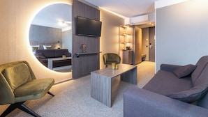 A modern living room with a round mirror, a flat-screen TV, a sofa, a coffee table, and a small side table. - Asteria Hotel Venray (Venray)