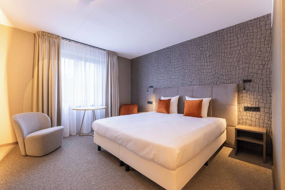 Ein Hotelzimmer mit einem großen Bett, einem Sessel, einem kleinen Tisch und einem Nachttisch.
