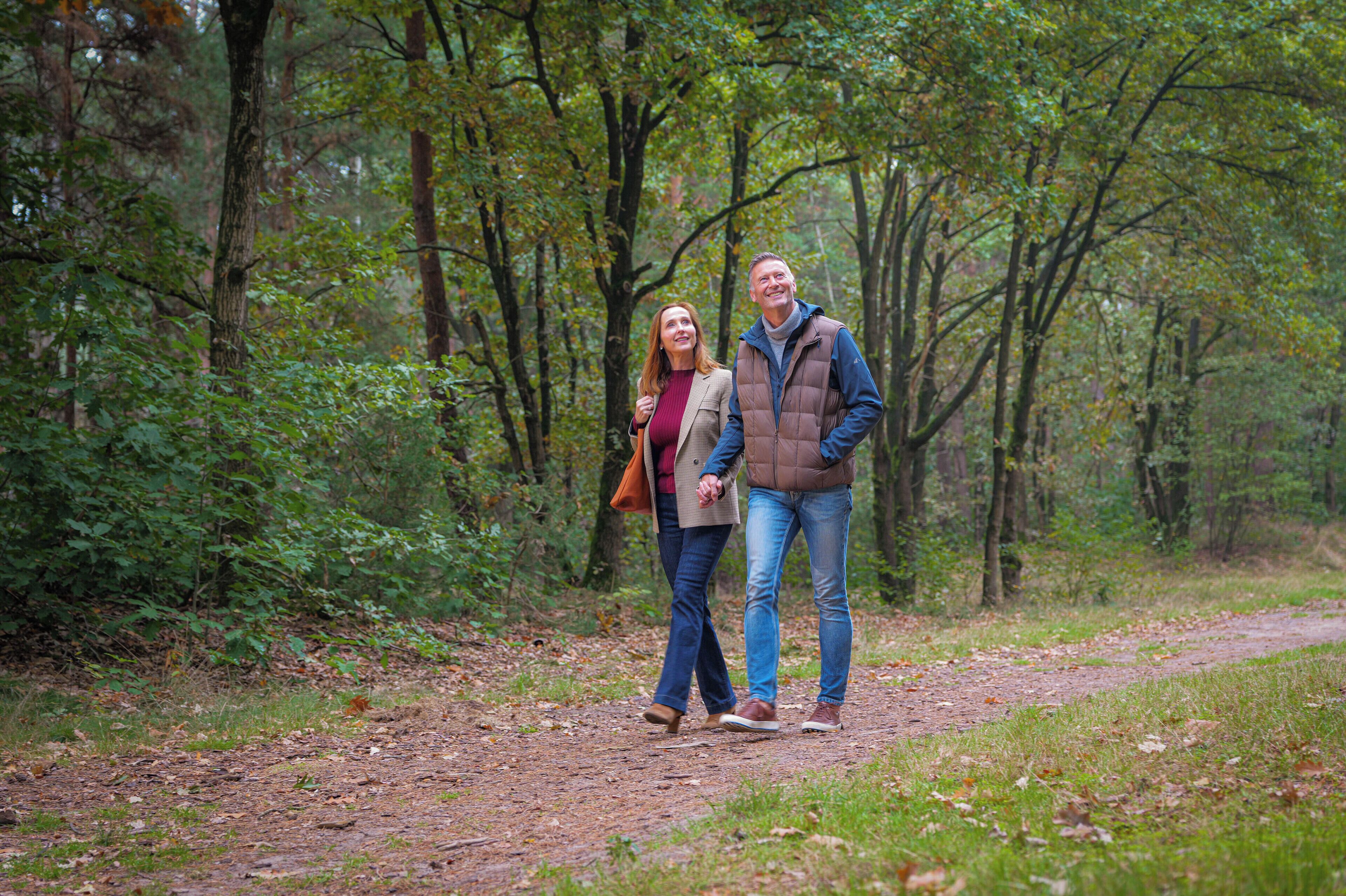 A couple walking on a forest path surrounded by trees.