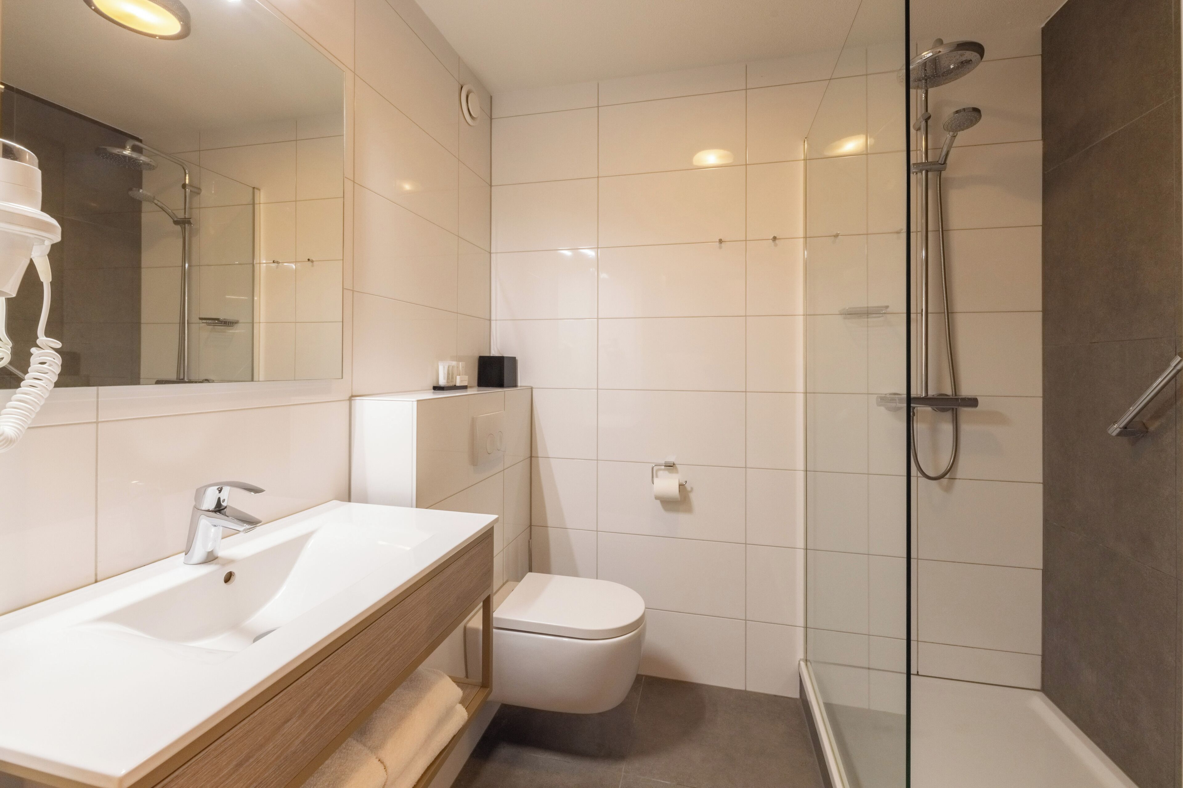 Um banheiro moderno com pia branca, vaso sanitário e área de chuveiro com box de vidro.