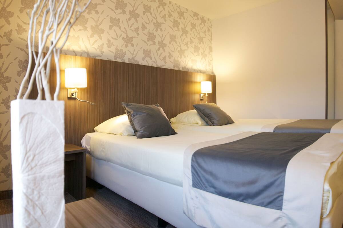 Ein Hotelzimmer mit einem Bett, zwei Nachttischen mit Lampen, einem Holz-Kopfteil und einem blumigen Wandmuster.