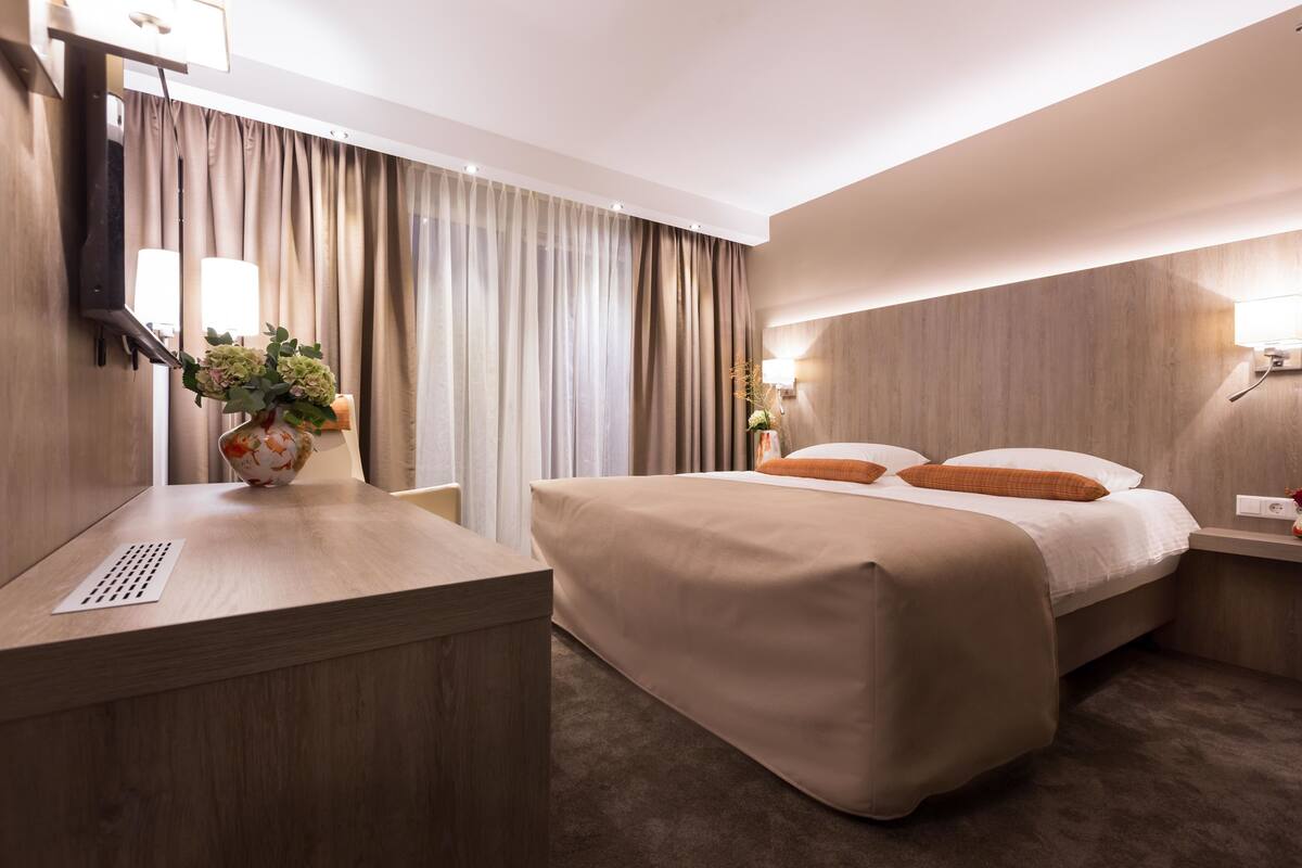A hotel room with a bed, bedside table, lamp, and curtains.
