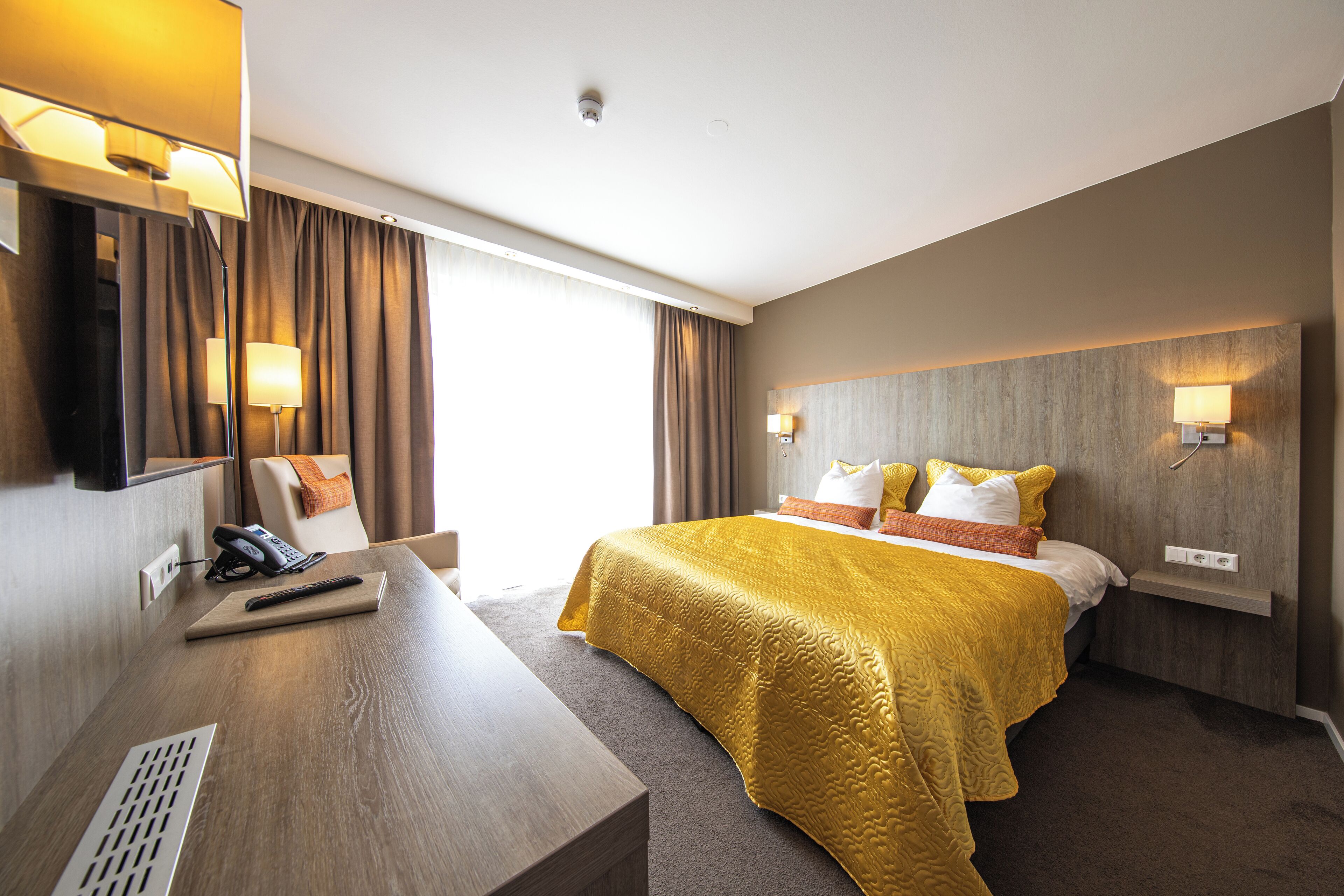 A hotel room with a bed, bedside table, lamp, and a mirror.