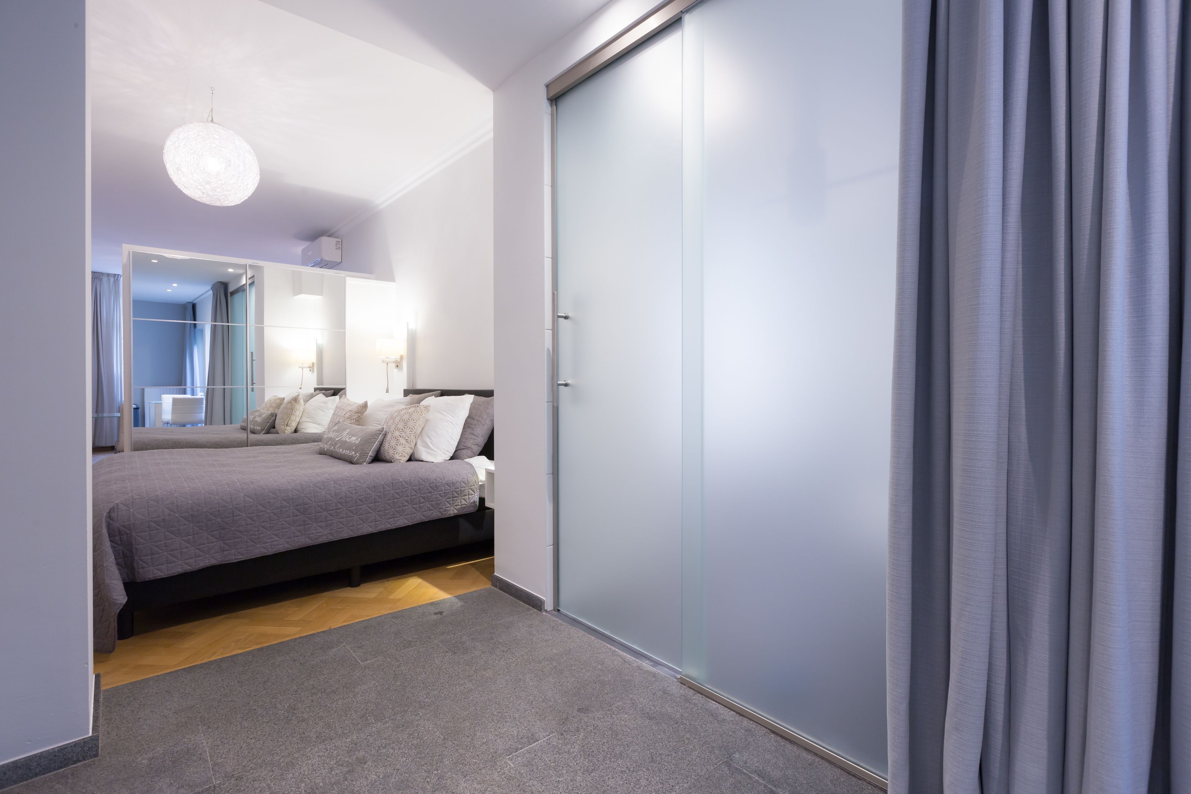 A modern bedroom with a bed, a wardrobe, and a mirror.