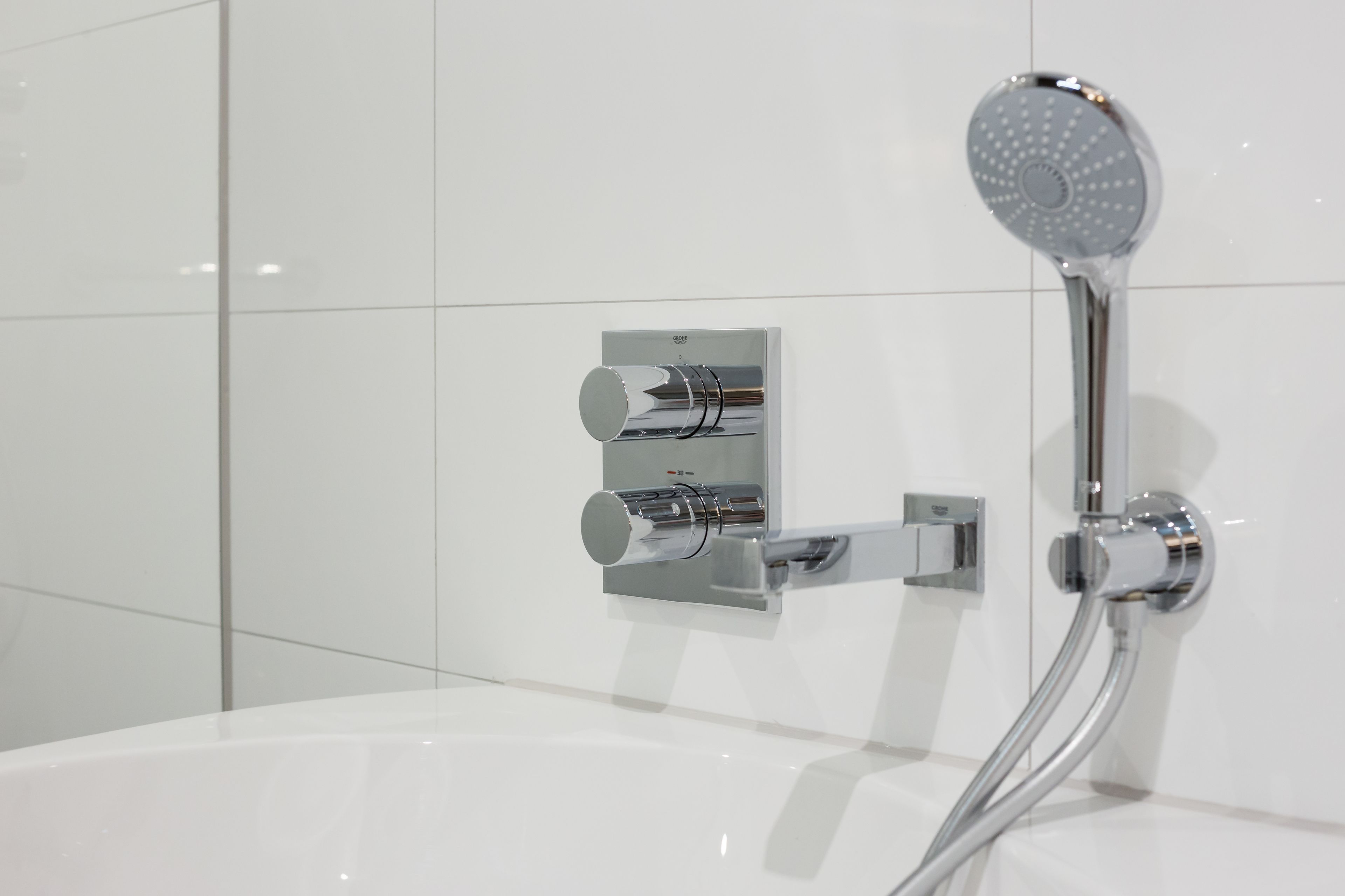 A modern bathroom with a chrome shower head, a wall-mounted control panel, and a white bathtub.