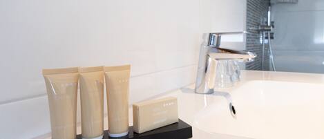 A hotel bathroom with a white sink, a mirror, and three toiletry bottles labeled "Hotel Scheepers" on a black tray.