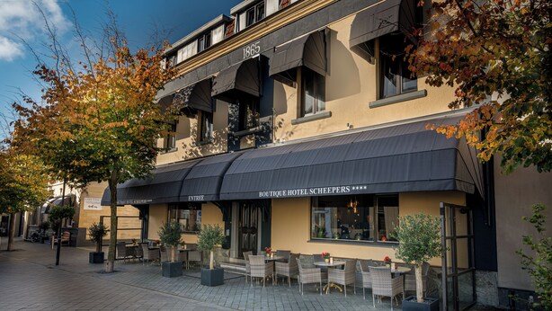 Un hotel boutique con mesas al aire libre, un letrero que dice "1865" y un cielo despejado.