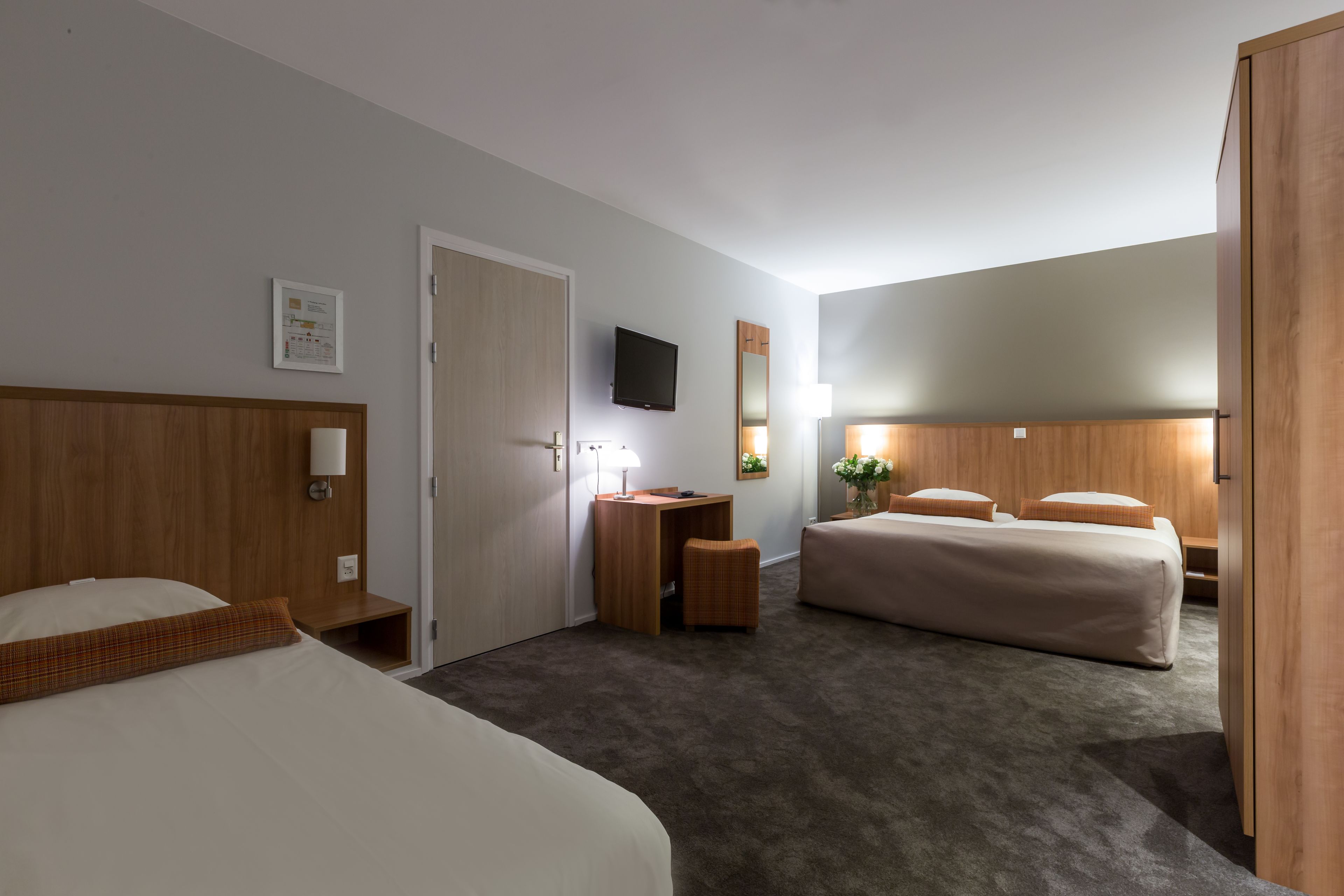 A hotel room with two beds, a desk, a television, and a mirror.