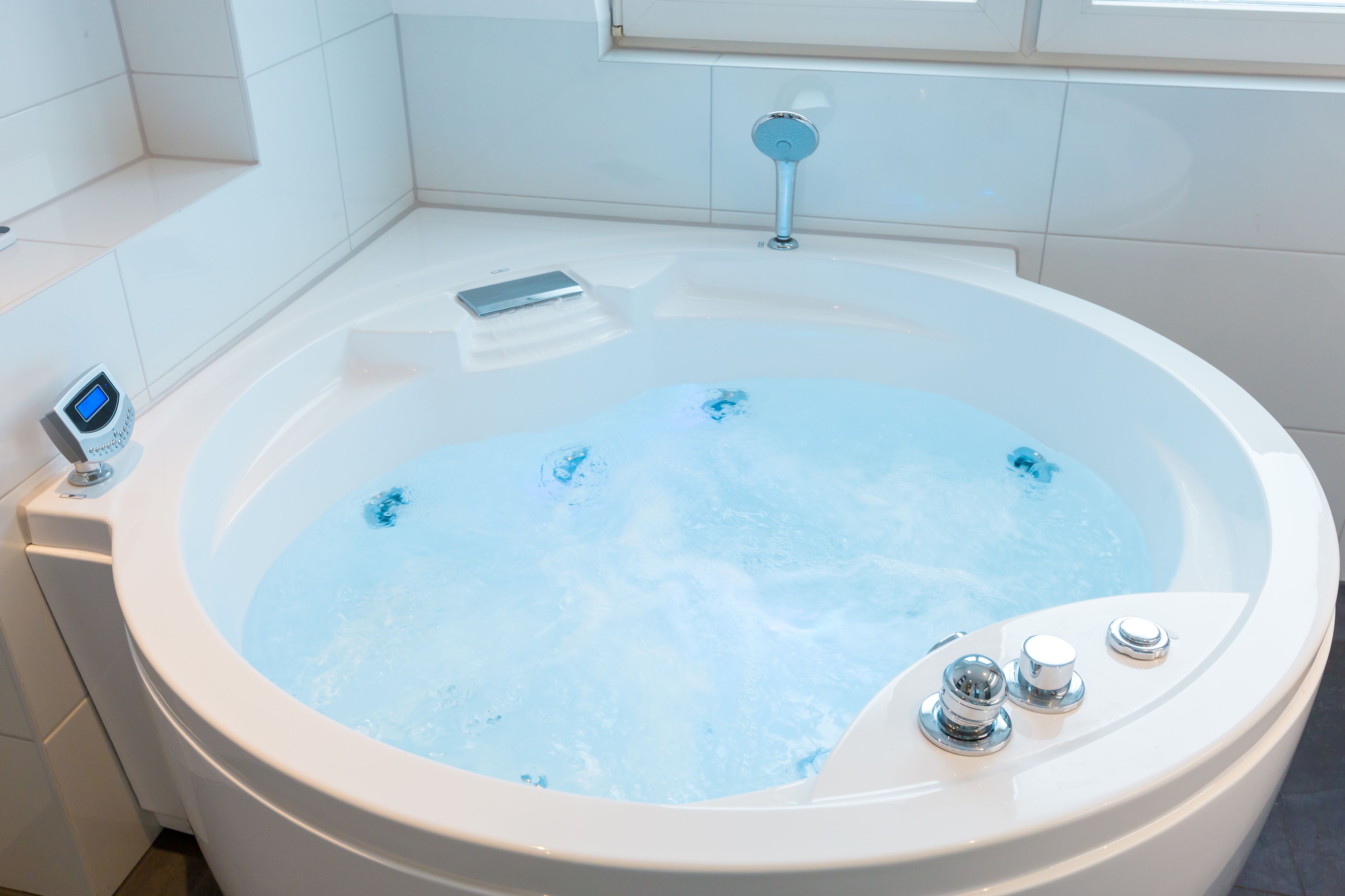 Une salle de bain moderne avec une grande baignoire, un panneau de commande numérique et une fenêtre située au-dessus de la baignoire.