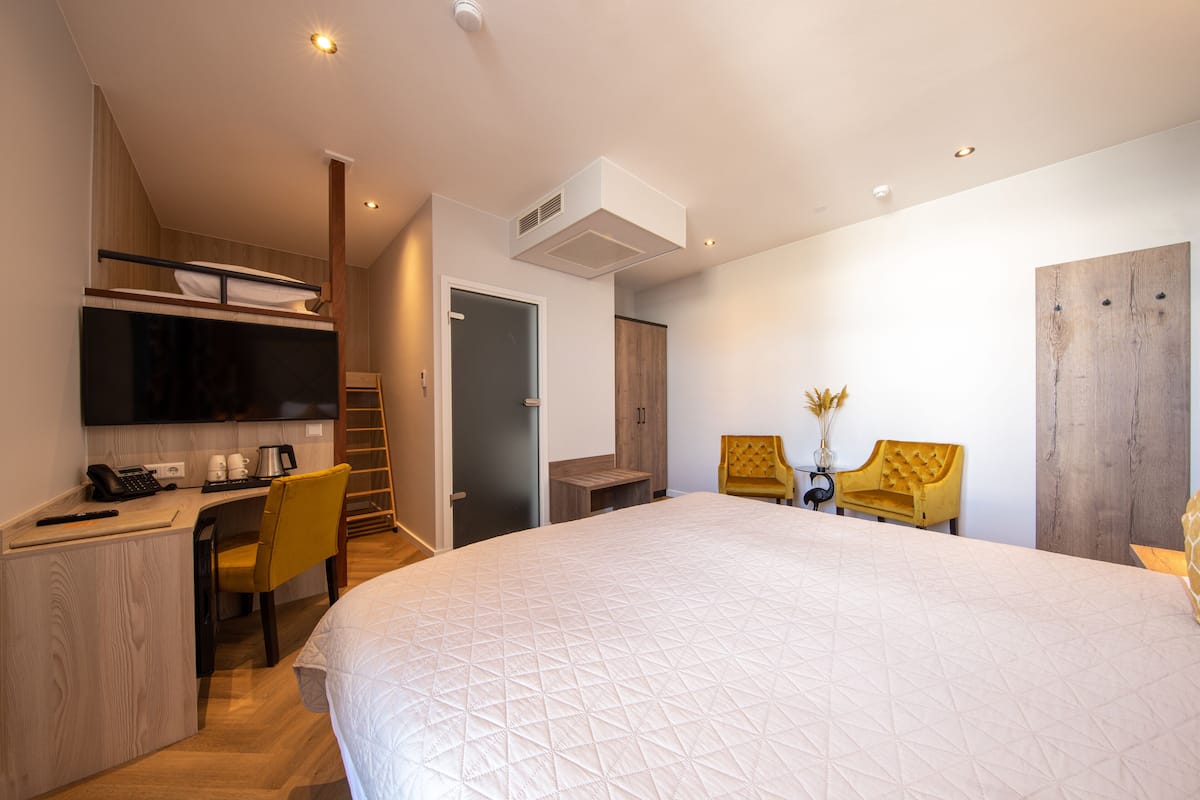 A modern hotel room with a large bed, a desk with a chair, a TV, and a wooden wardrobe.