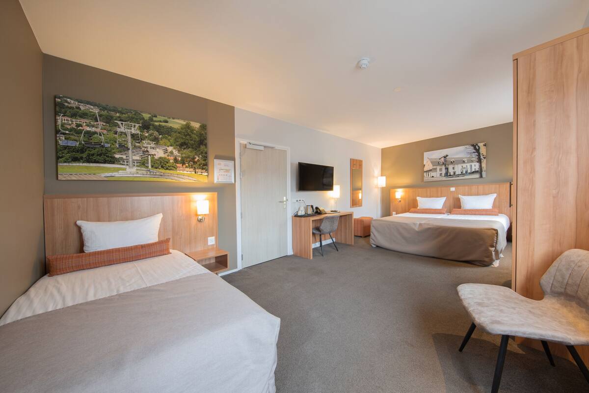 A hotel room with two beds, a desk, a chair, and a TV.