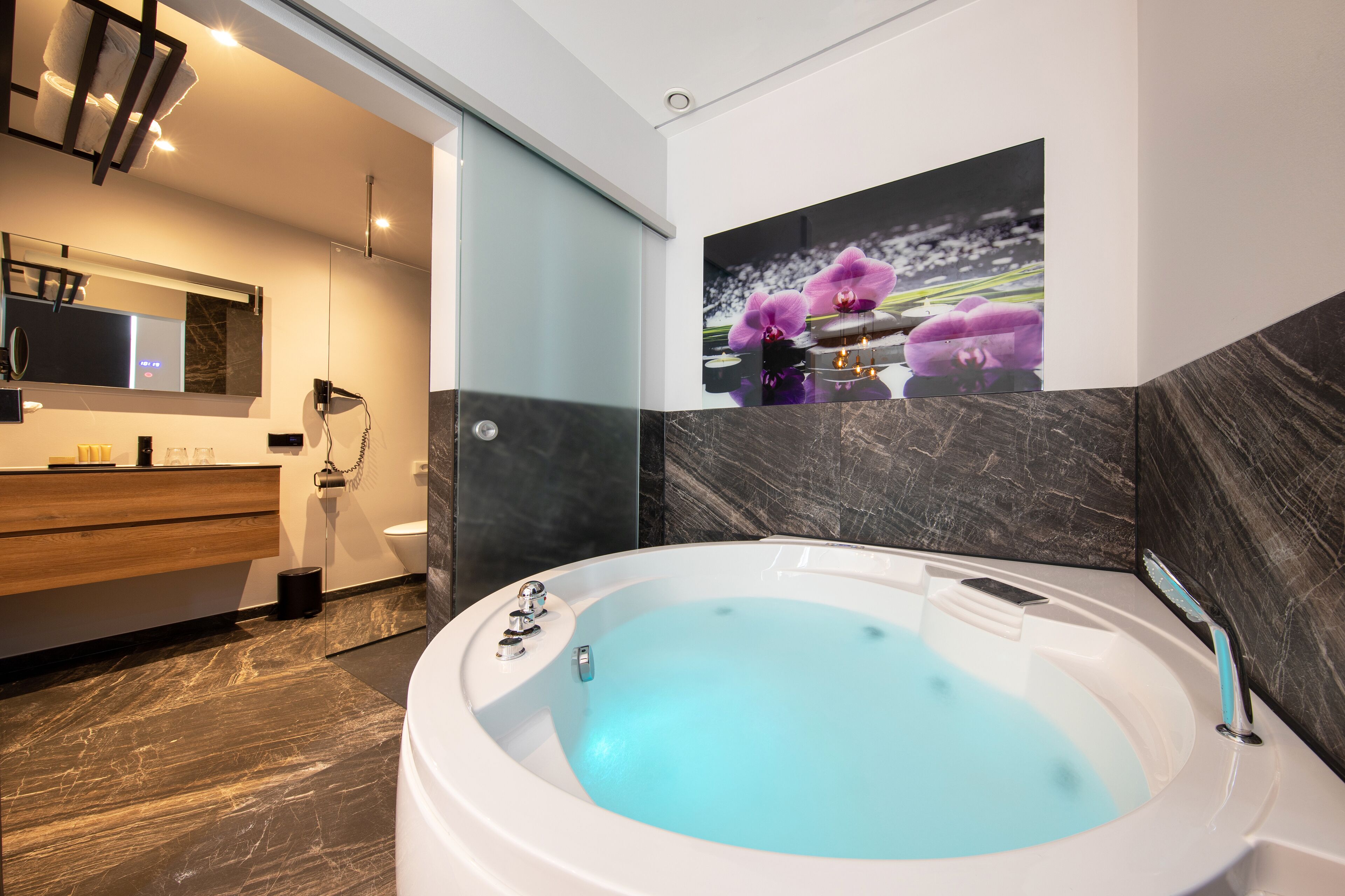 Un baño moderno con una bañera grande, un tocador de madera, un espejo y un inodoro empotrado.