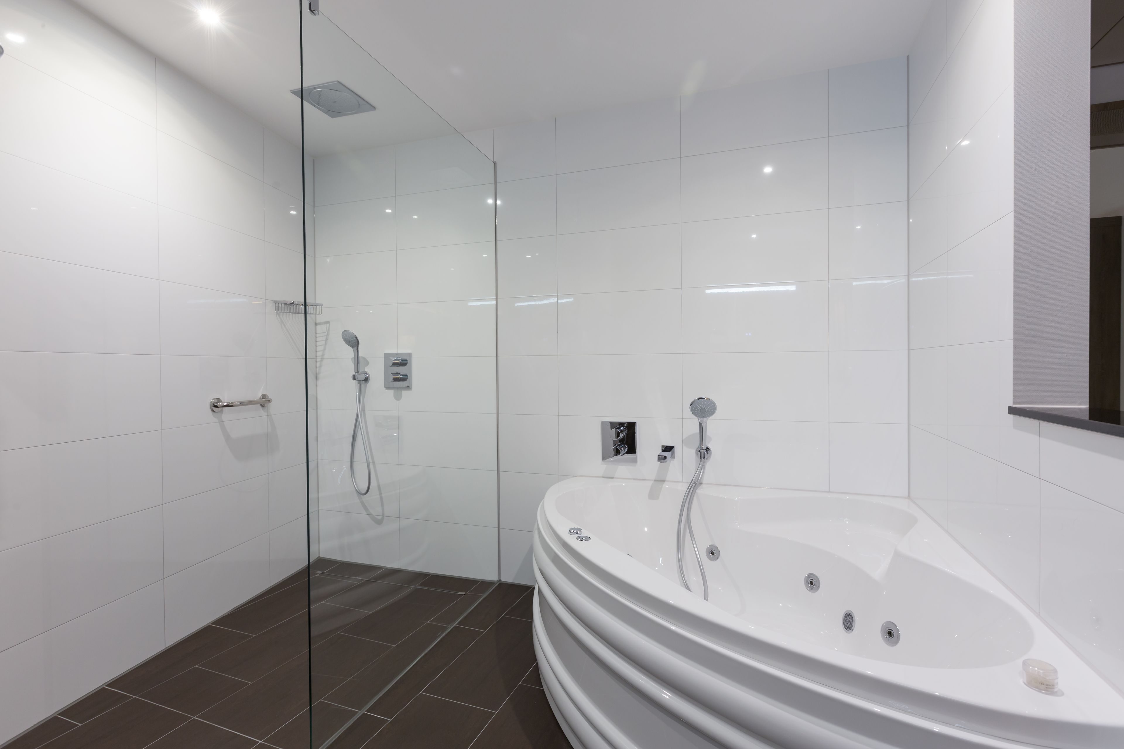 A modern bathroom with a glass-enclosed shower, a freestanding bathtub, and white tiled walls.