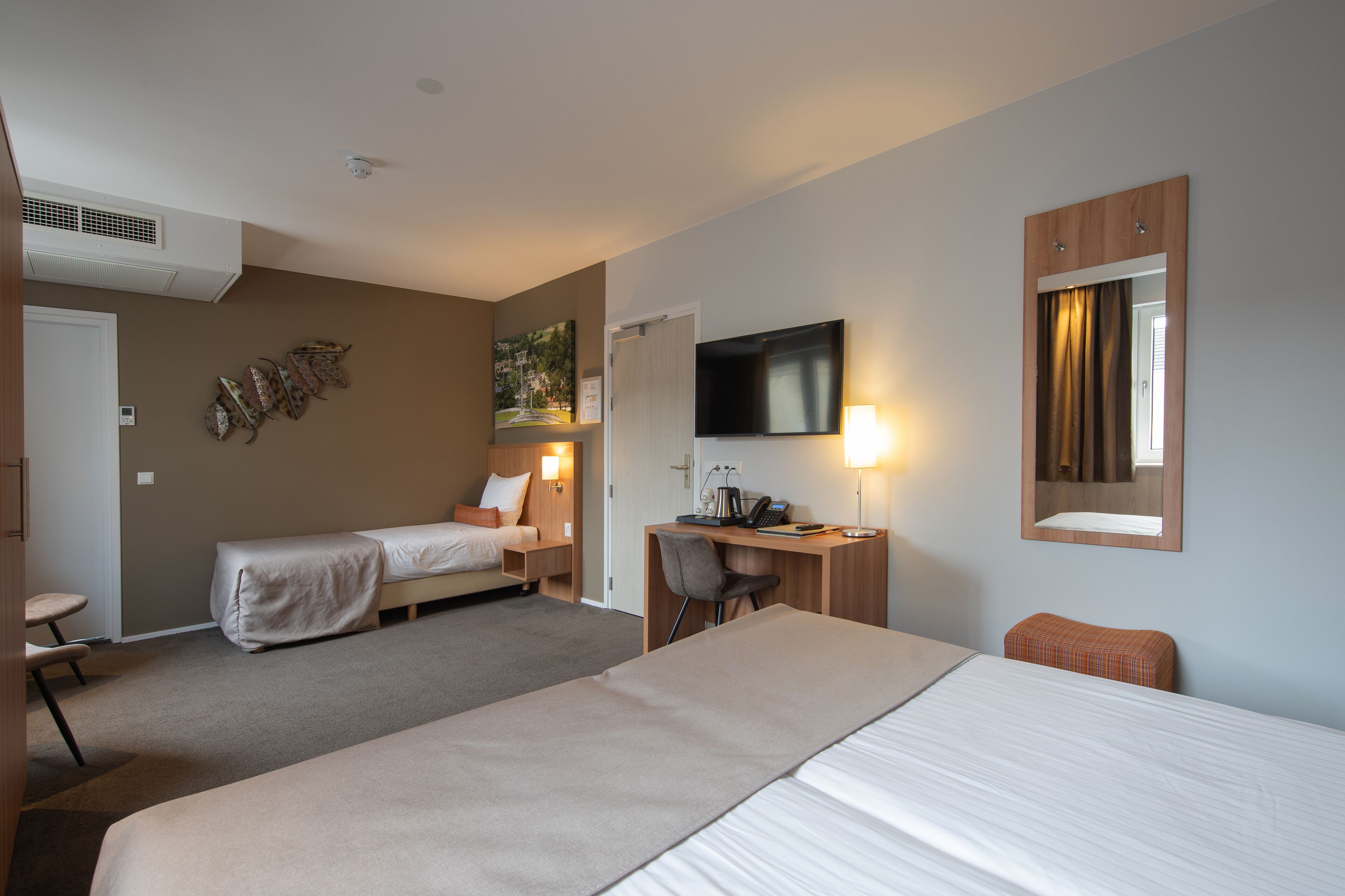A hotel room with two beds, a desk, a chair, a TV, and a mirror.