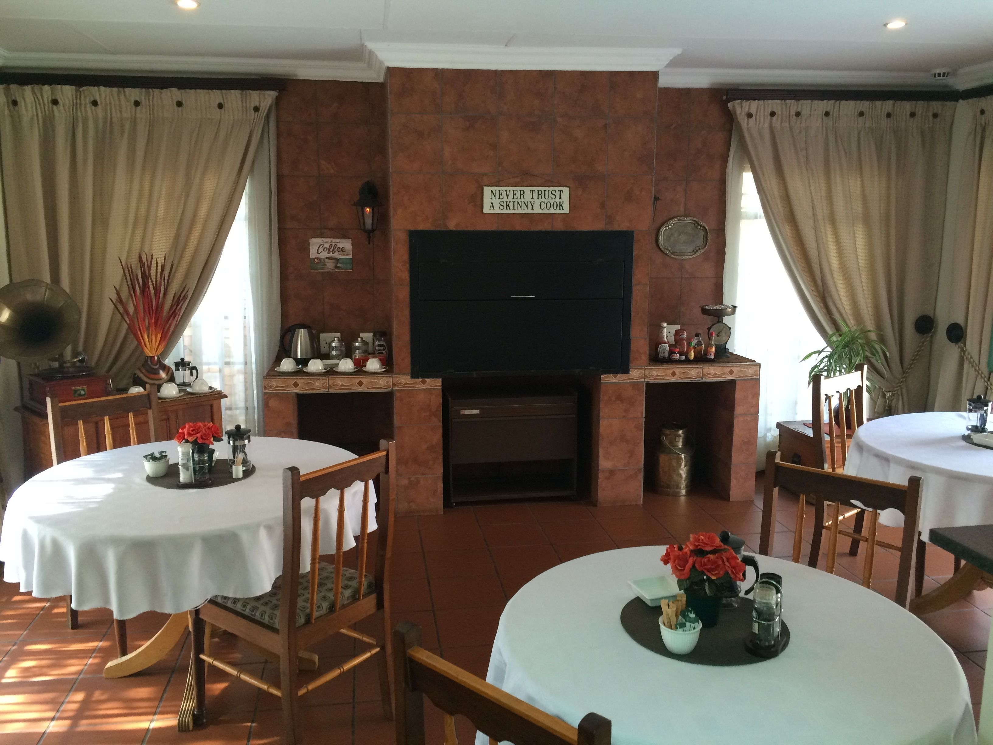A dining area with two round tables, chairs, a television, and a sign above the fireplace.