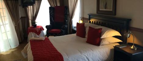 A hotel room with a large bed, a chair, a TV, and a fireplace.