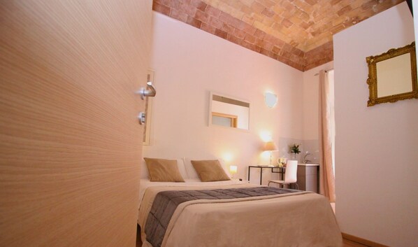 Una habitación de hotel con cama, mesita de noche, lámpara y espejo en la pared.