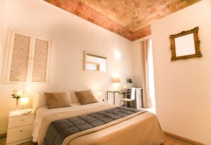 Un dormitorio con cama, mesita de noche, lámpara y un escritorio con silla.