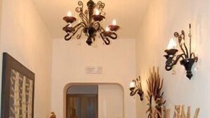A hallway with a chandelier, a white vase with dried plants, and a patterned rug. - Trastevere Relais (Rome)