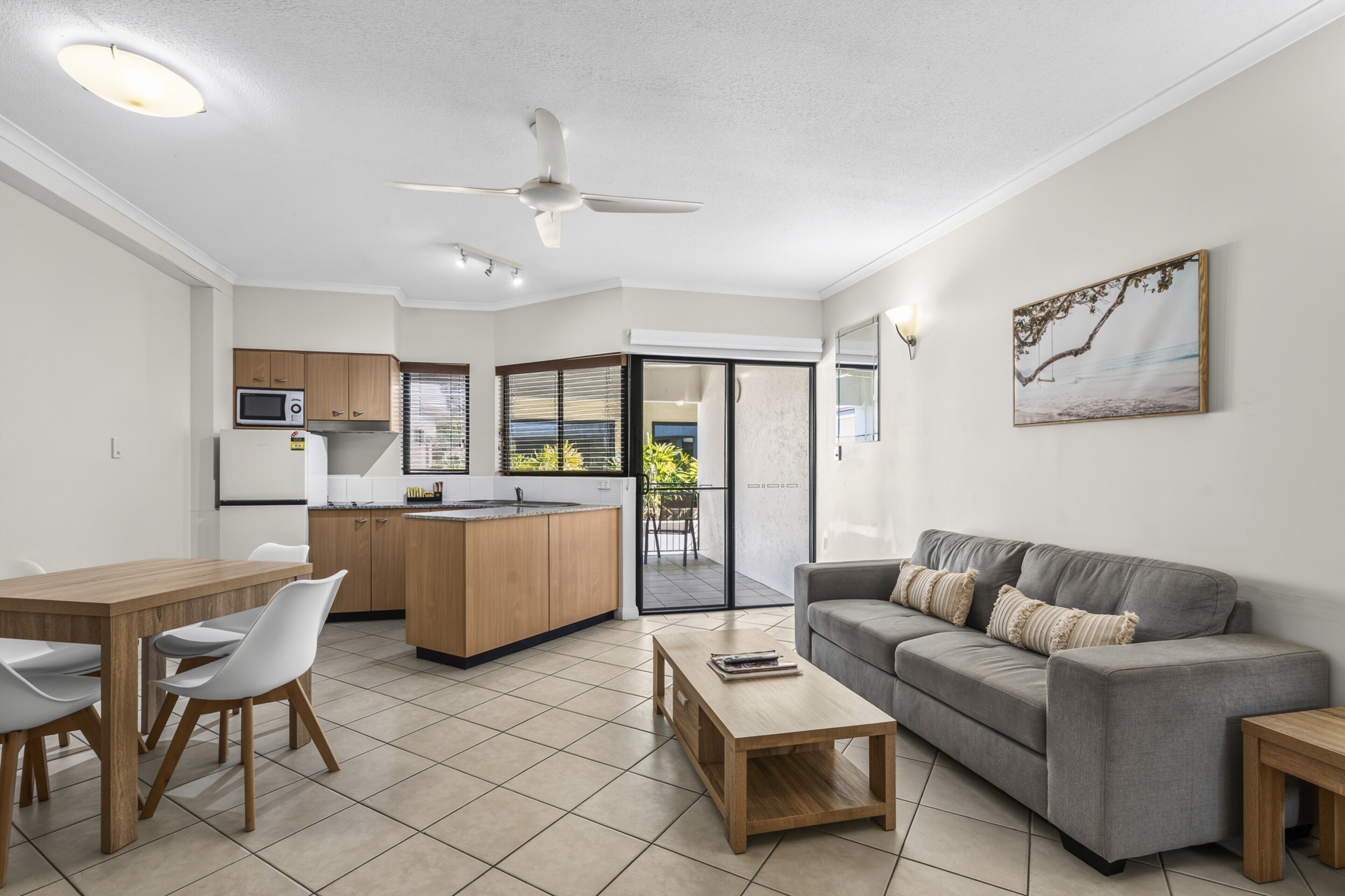 A modern kitchen with a dining area, a grey sofa, and a ceiling fan.