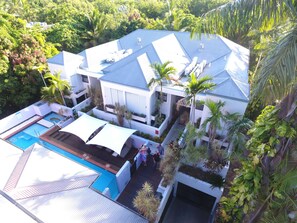 Vista aérea de una casa moderna con piscina, rodeada de exuberante vegetación y palmeras.