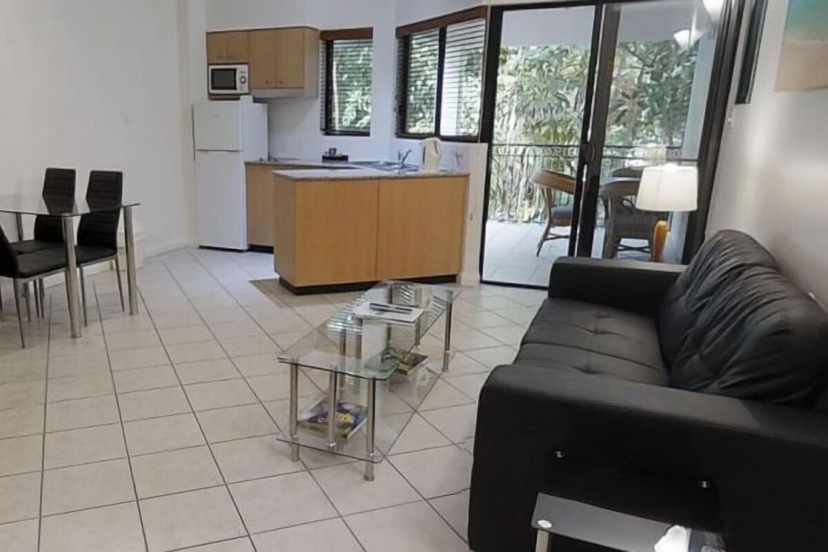 A compact living space with a dining area, a kitchenette, a glass-top coffee table, and a sofa.
