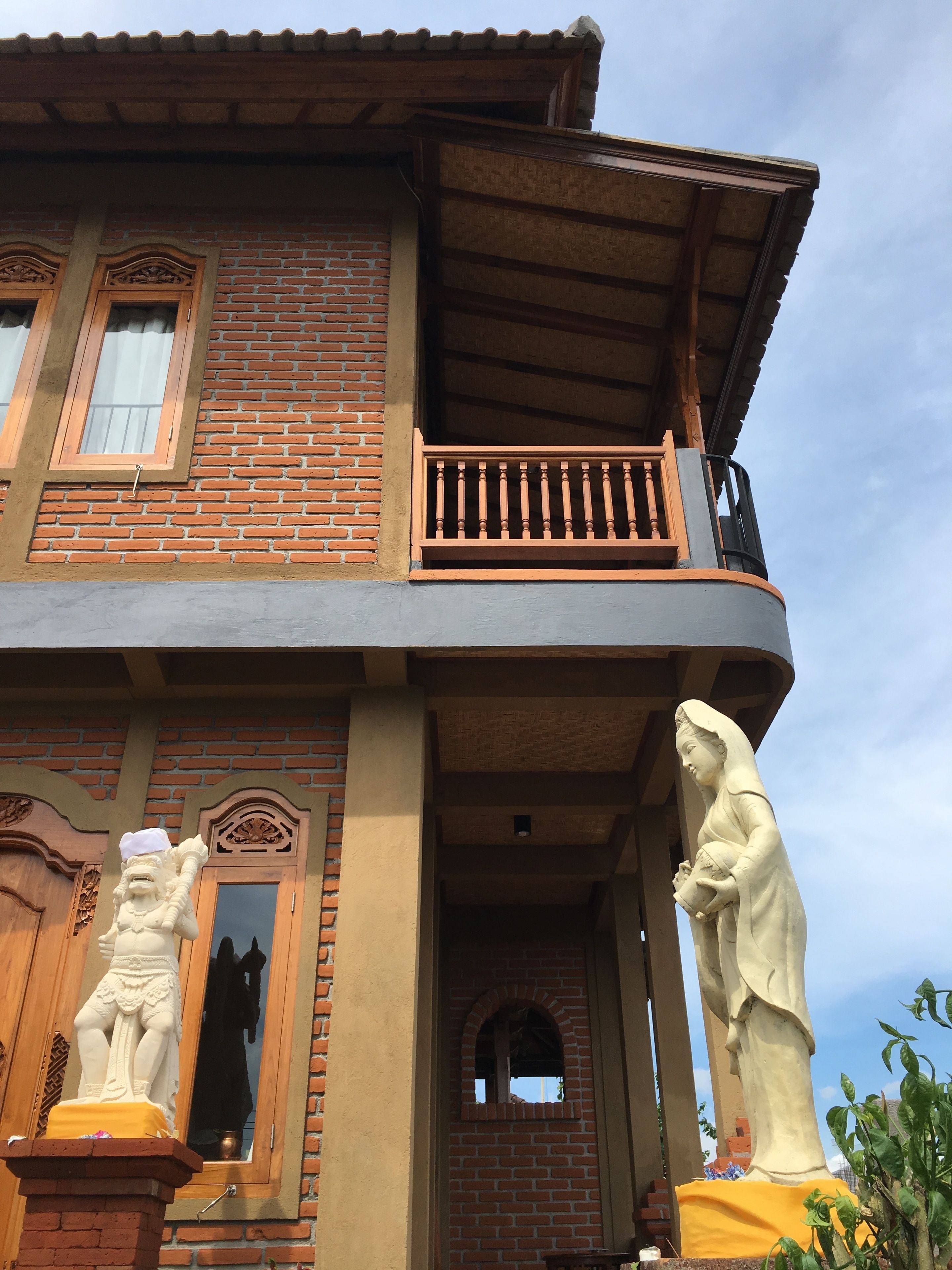 A two-story building with a balcony, a statue, and a window with a decorative frame.