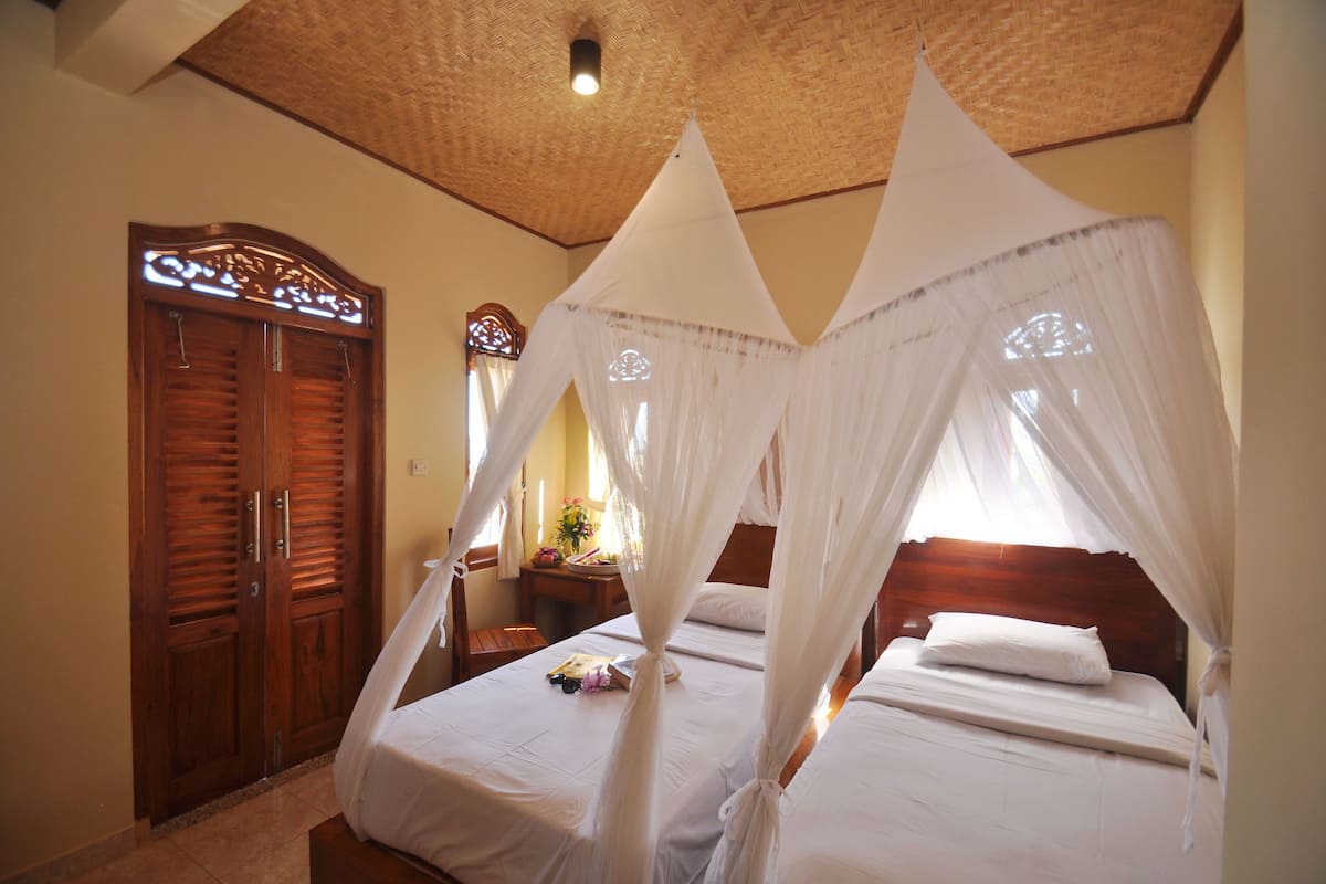 A room with two beds, one with a canopy. There is a wooden wardrobe and a nightstand with a lamp.