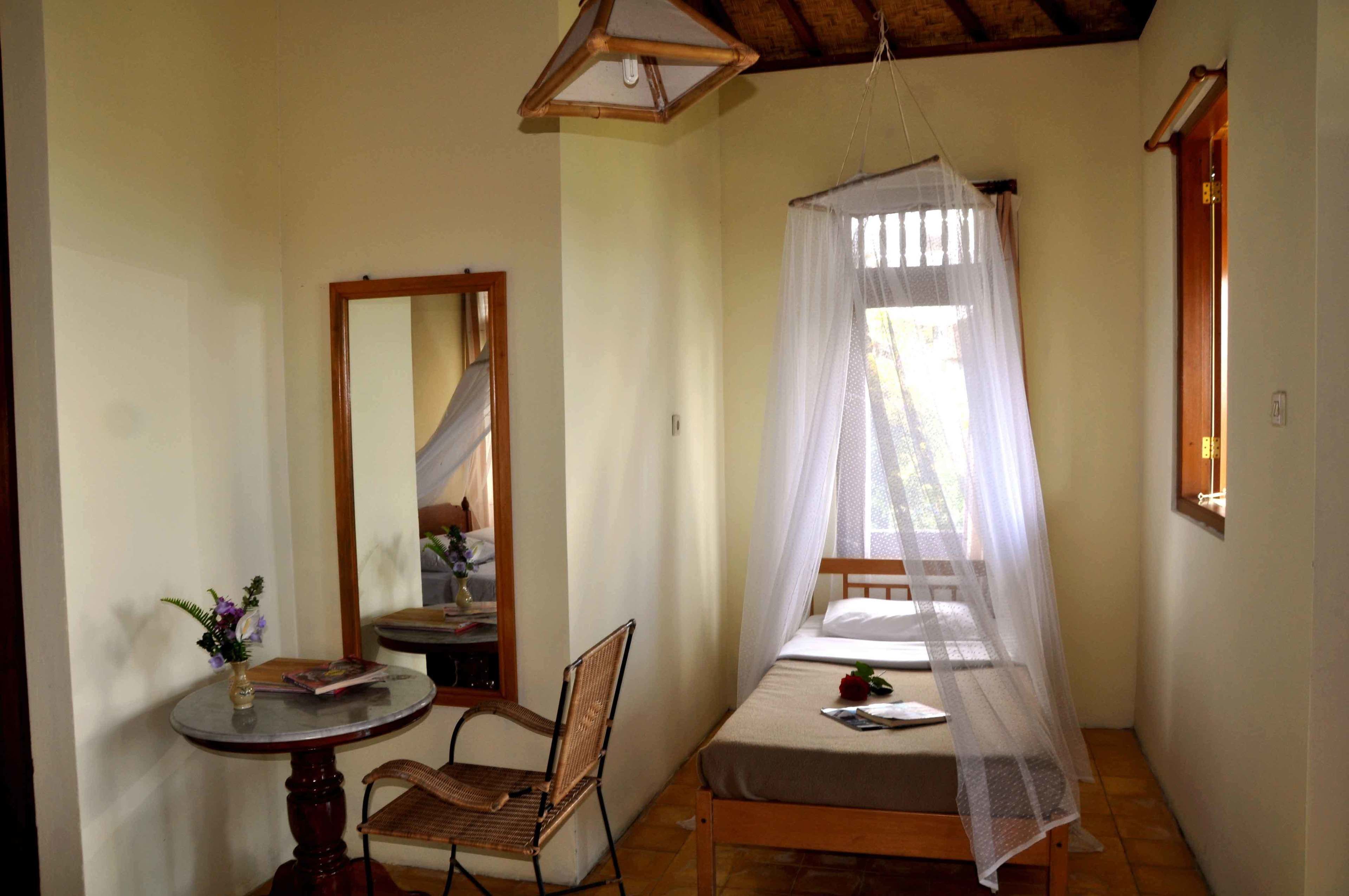 Um quarto pequeno e acolhedor com uma cama de solteiro, uma cadeira, uma mesa e um espelho.