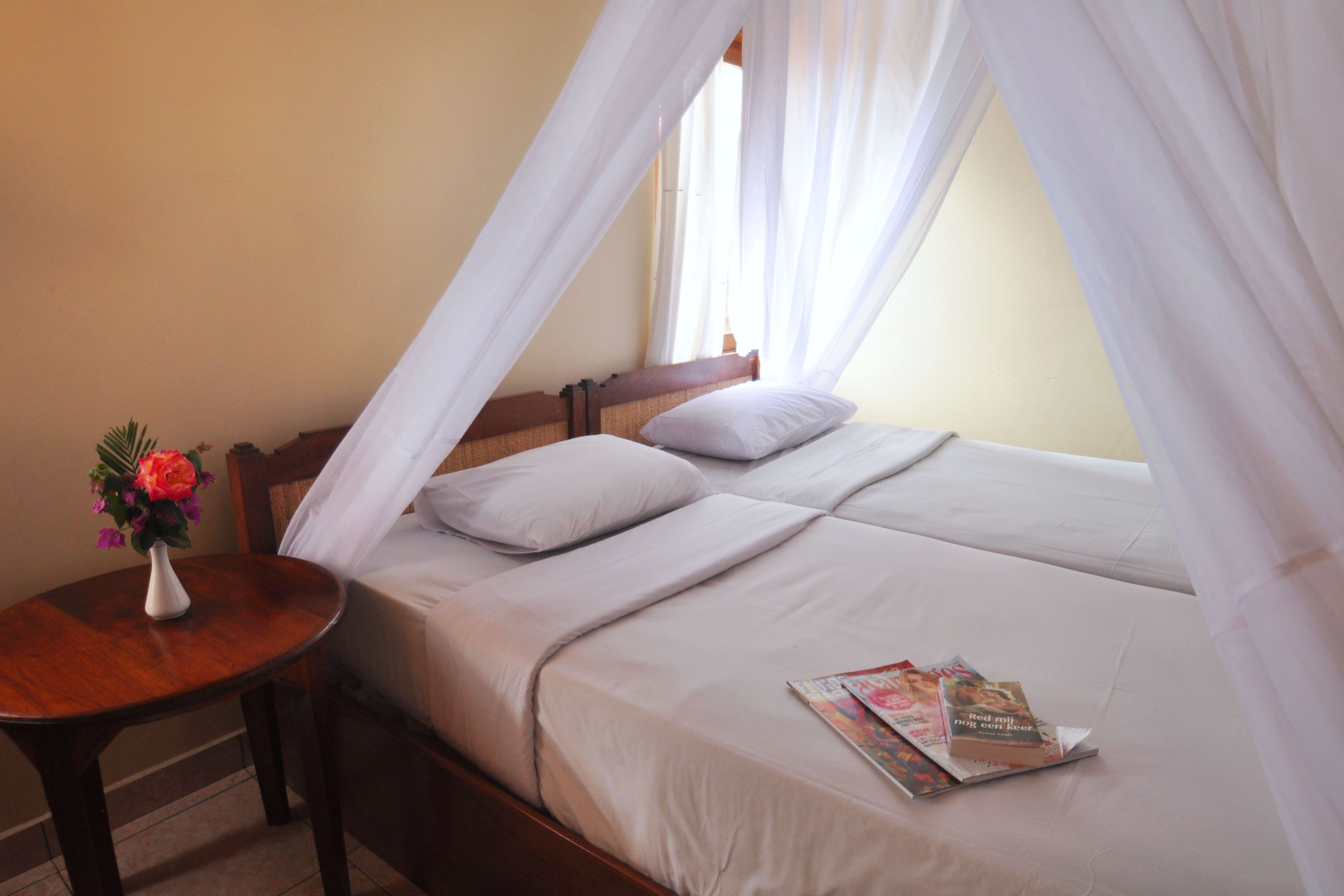 Una cama con dosel, una mesita de noche con un florero y una ventana con cortinas.