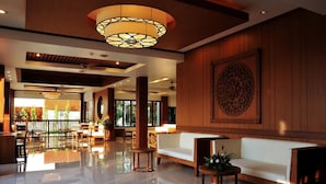 Um hall espaçoso com piso refletivo, uma grande parede de madeira com painel decorativo e uma área de estar com sofá branco e mesa redonda com arranjo de flores.